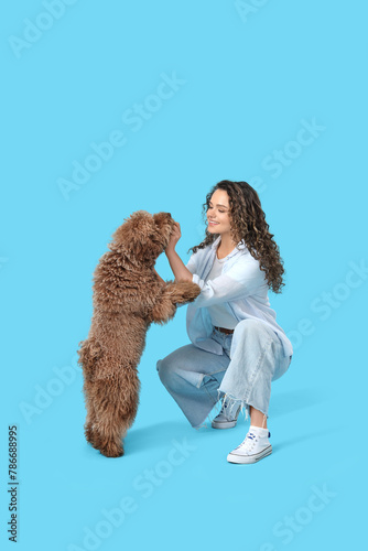 Young woman with cute poodle on blue background