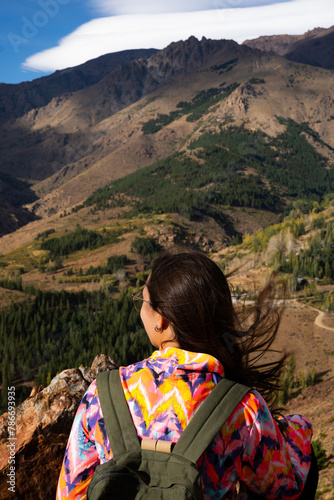 Young Latina woman with sportswear and backpack on her back looking at a mountain landscape in Patagonia Argentina. Vertical photo.