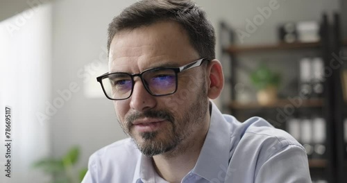 Smiling businessman entrepreneur working online on computer at home desk, laptop screen reflecting in glasses. Successful entrepreneur working on innovation startup, analyzing financial data