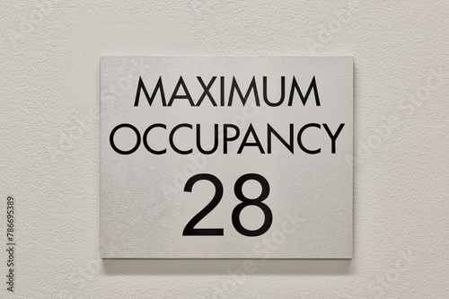 Fényképezés Maximum Occupancy sign on white interior wall in commercial building, 28 capacity copy space