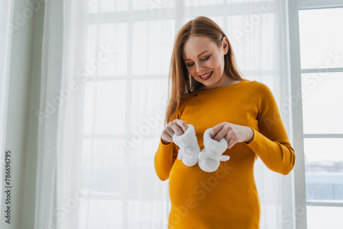 Pregnancy motherhood people expectation future. Pregnant woman with big belly holding newborn baby booties smiling at home. Young mom enjoying pregnancy. Maternity tenderness parenthood new life