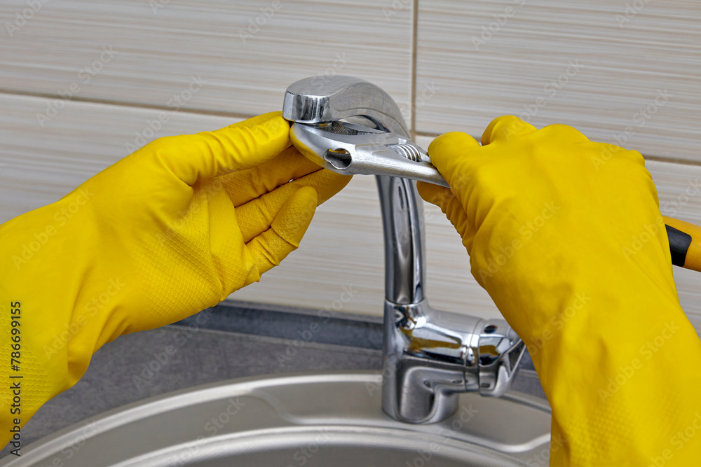 Fototapeta premium Repairman in yellow gloves with an adjustable wrench changes the faucet aerator