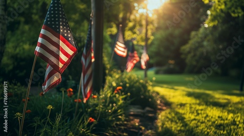 A row of American flags proudly displayed among green shrubbery, bathed in the warm sunlight of a clear day..