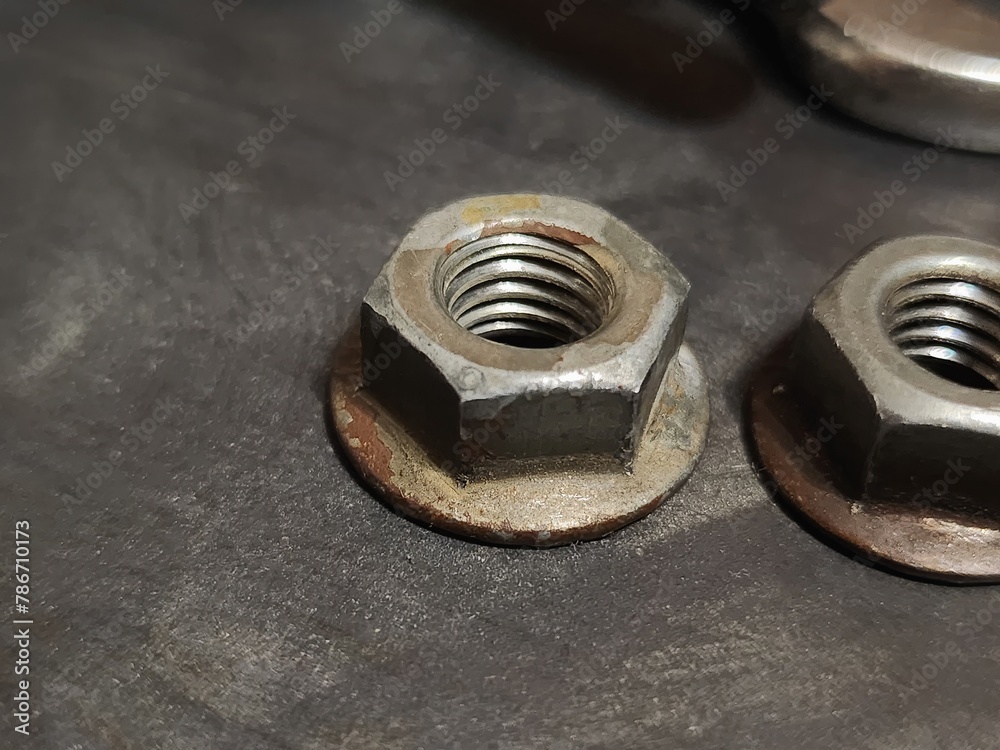 Close-up view of two weathered nuts and bolts with visible oxidation and wear patterns on a dark textured surface, showcasing the effects of time and use on metal hardware components