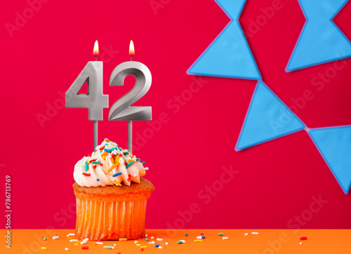 Number 42 candle with birthday cupcake on a red background with blue pennants