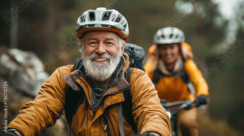 Older man wearing a bicycle helmet and a yellow jacket, smiling while riding a bike. Another person is blurred in the background, also riding a bike.