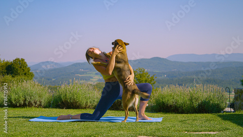 Lively dog jumps and hugs a lady practicing crescent lunge yoga pose in garden