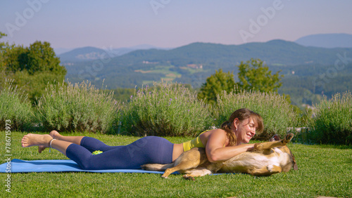 Naughty dog disturbs woman holding a plank pose during yoga workout in garden
