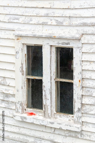 A four pane clear glass window with dirt and grime. The antique window is in a white wooden house with paint peeling. There are rusty nails in the horizontal boards and red paint on the sash.  © Dolores  Harvey