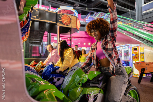 African American teenage girl celebrates victory in the arcade motorcycle race with her multiethnic friends