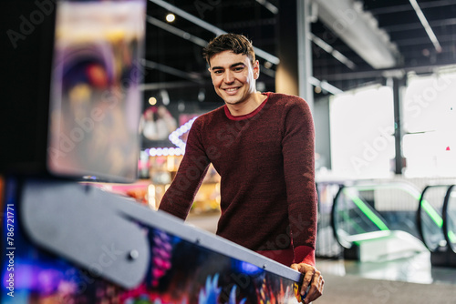 Photos Portrait of a smiling handsome young man leaning on a pinball machine in an arca