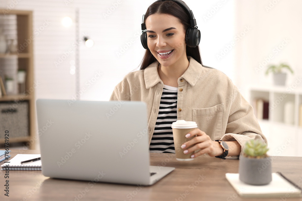 Young woman in headphones watching webinar at table in room Young woman in headphones watching webinar at table in room