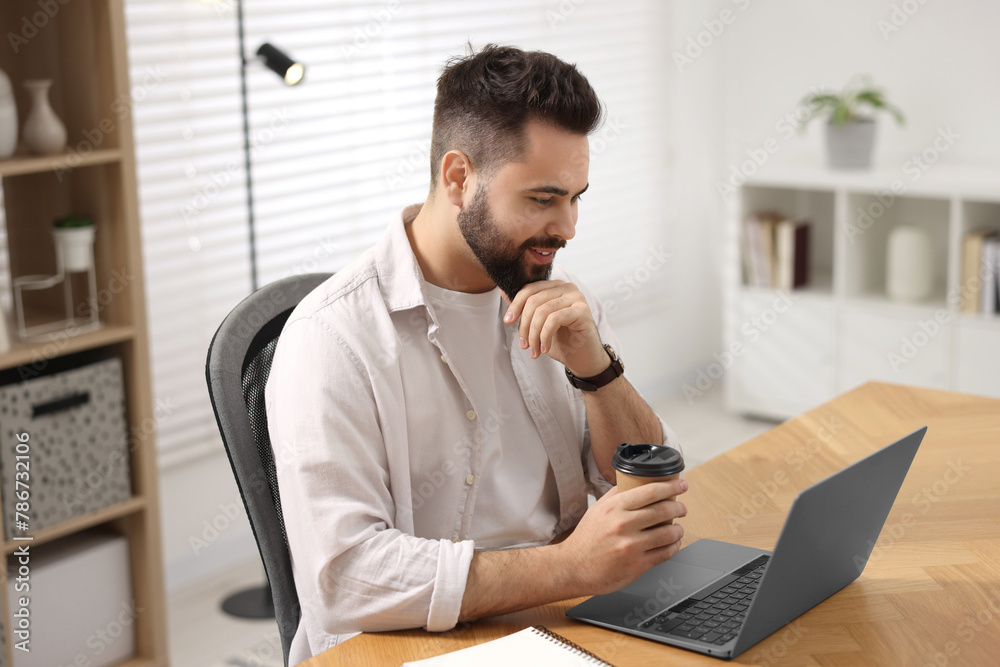 Young man with cup of coffee watching webinar at table in room Young man with cup of coffee watching webinar at table in room