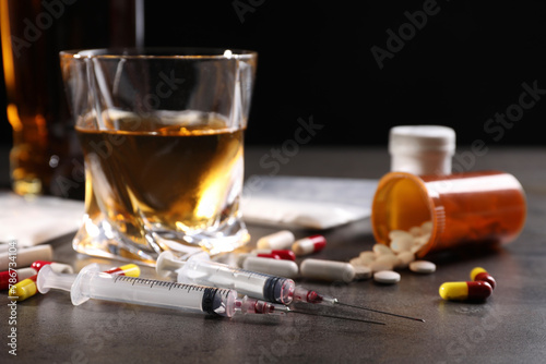 Alcohol and drug addiction. Syringes, whiskey in glass and pills on grey table, closeup photo