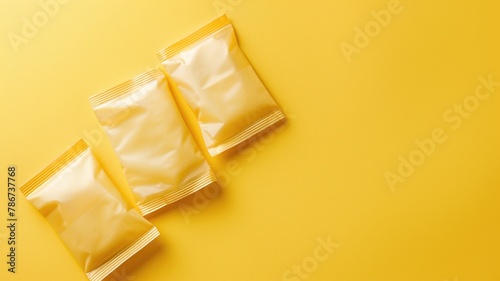 Three sealed, unbranded yellow packets on background © Artyom