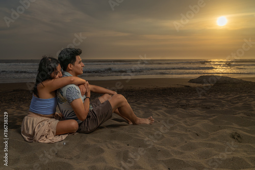 Couple in love sitting on the sand embracing looking at the sea