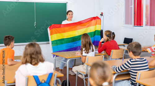 Positive female teacher explaining lgbt theme to children during lesson in class in secondary school photo