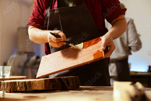 Woodworking specialist applying varnish on wood to build up protective layer. Carpenter in assembly shop lacquering wooden board after sanding surface to ensure smoothness, close up shot photo