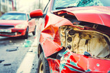 Close-up of a red car with significant front-end damage after a collision, debris scattered on the road.