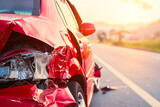 Close-up of a red car with significant front-end damage after a collision, parked on a roadside during sunset.
