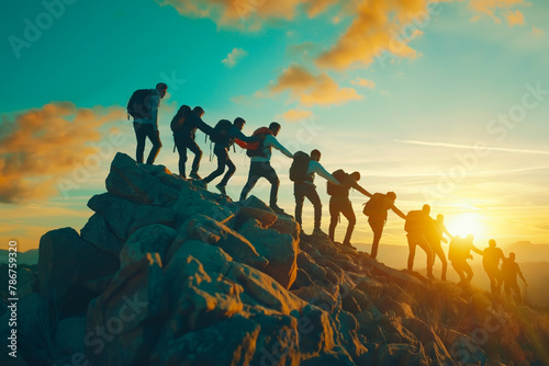 Panoramic view of team of people holding hands and helping each other reach the mountain top in spectacular mountain sunset landscape