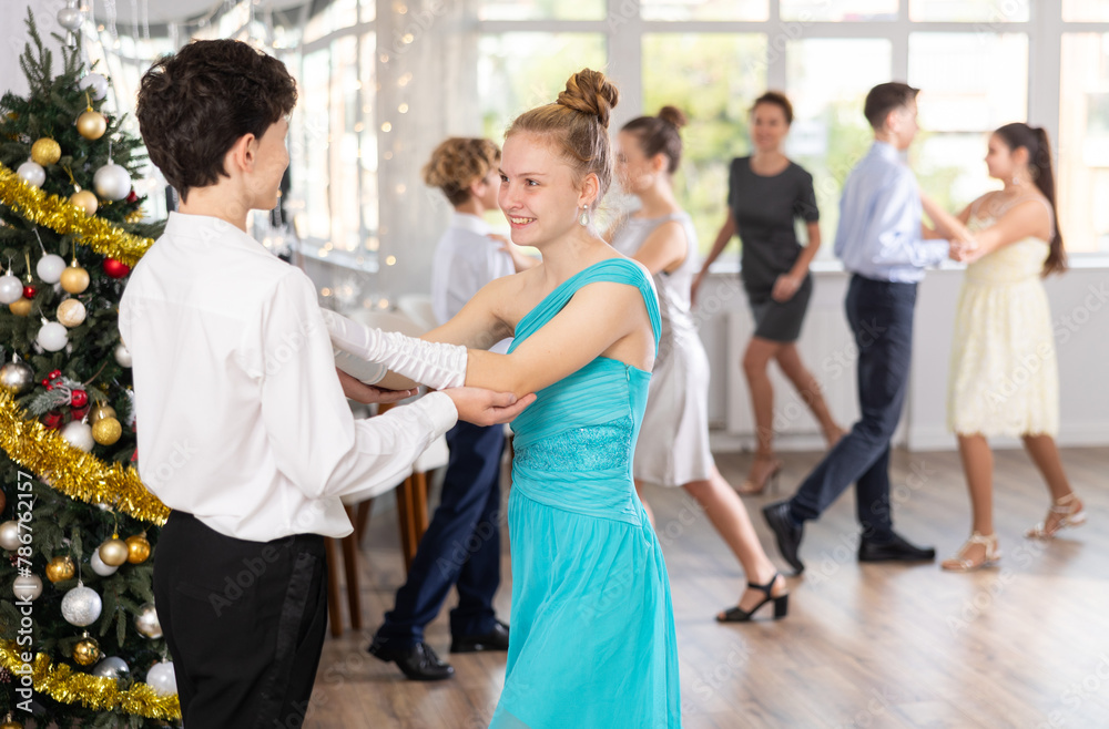 Smiling teenage girl enjoying slow dance with friend at school event during festive Christmas party with group of peers..