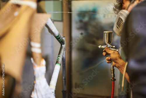 Man wearing a protective respirator mask spray painting a bicycle frame in his workshop. Selective focus composition. Real people working.