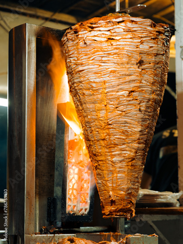 Vertical image Grilling traditional trompo al pastor street taco pork meat on spit with flames at night in Mexico.