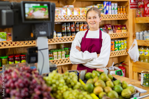 Fotografie Positive girl who works part-time as a trainee saleswoman at the checkout counte