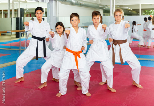 Teenager children wearing karate uniform fighters poses in white kimono during group training in gym
