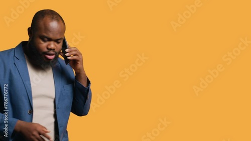 African american man enjoying talking with friends phone call using smartphone, studio background. BIPOC person walking around conversating during telephone call, camera A photo