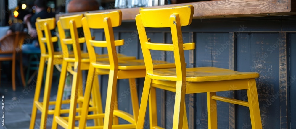 Multiple bright chairs in yellow color placed neatly in rows along a wooden counter inside a bar Multiple bright chairs in yellow color placed neatly in rows along a wooden counter inside a bar