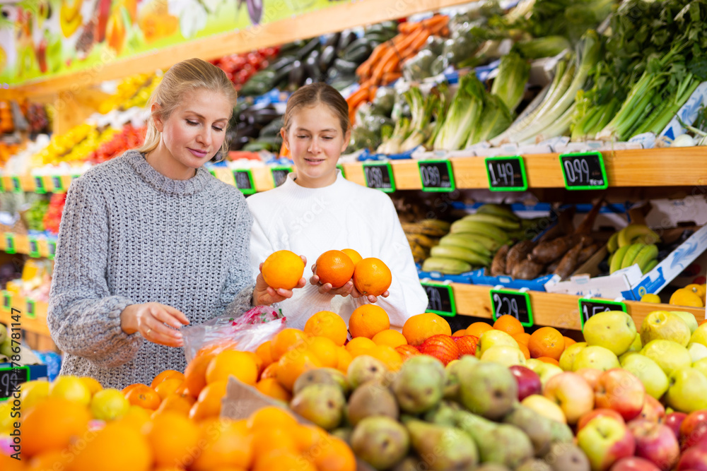 Woman with teen daughter who came to the supermarket for shopping, choose oranges at the counter