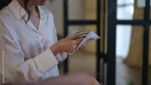 Close-up. Two unrecognizable women pass each other a paper envelope with hundred-dollar American bills. The woman opens the envelope and looks at the money photo