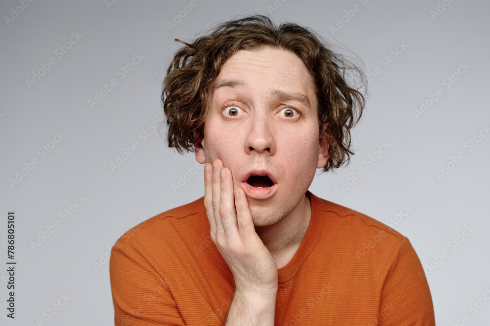 Medium closeup studio portrait of young Caucasian man with wavy hair looking at camera showing surprise emotion, copy space Medium closeup studio portrait of young Caucasian man with wavy hair looking at camera showing surprise emotion, copy space