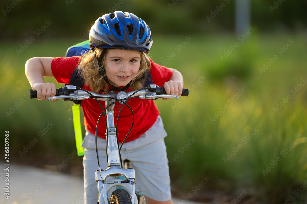 Naklejka premium Little kid boy ride a bike in the park. Kid cycling on bicycle. Happy smiling child in helmet riding a bike. Boy start to ride a bicycle. Sporty kid bike riding on bikeway. Kids bike.