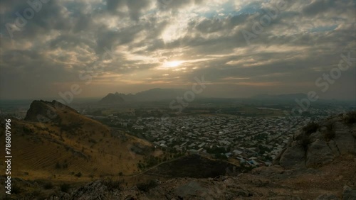 Timelapse of clouds over the Osh city. Skyline panoramic view at sunset over rooftops in small city in afternoon, golden hour time. View of Osh city  from the Sulaiman Too mountain, Kyrgyzstan. 
