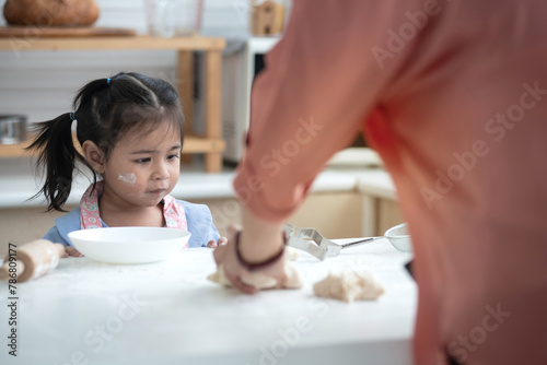 Little girl was playing with the bread dough that was placed on the table, she looked and wanted to try making bread like her mother, selective focus