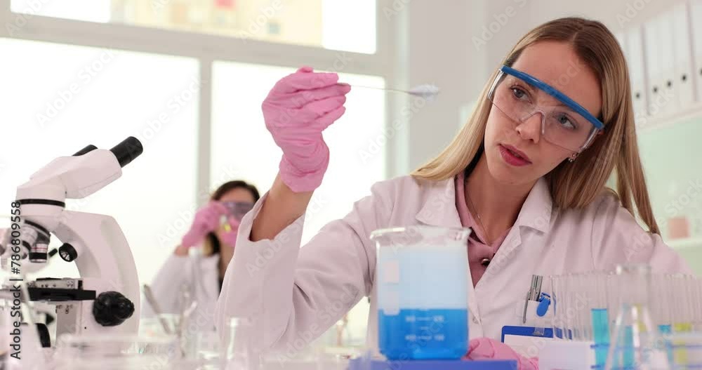 Woman wearing goggles collects foam from glass container in lab