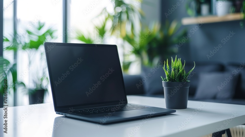 A laptop is open on a table next to a potted plant A laptop is open on a table next to a potted plant