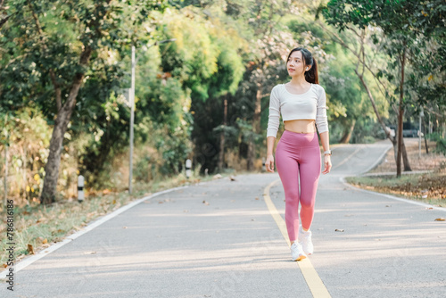 Woman in a white cropped top and pink leggings walking on a park path with green trees on the sides.
