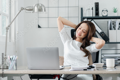 Relaxed professional woman takes a break to stretch at her workstation  signaling a moment of well-deserved rest in her busy day.