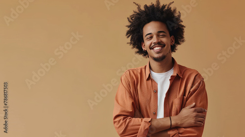 Portrait of smiling young man with afro hair wearing terracotta shirt paired with white t-shirt, with folded hands isolated on beige background photo