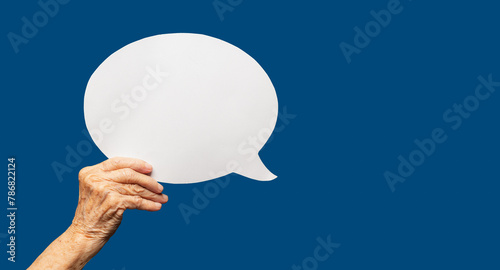 Close-up of a senior woman's hand holding a blank white speech bubble against a blue background.