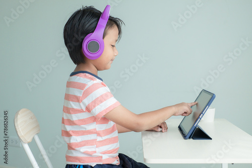 Asian boy uses finger tab on the tablet screen while learning online class