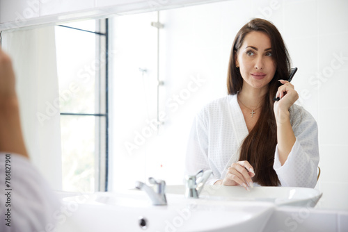 young woman combing hair in front of mirror at bathroom © offsuperphoto