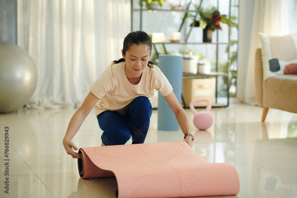 Woman rolling out yoga mat to exercise at home Woman rolling out yoga mat to exercise at home