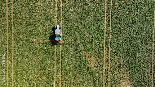 Top-down aerial shot of a tractor spraying in a lush green field with distinct track lines. photo