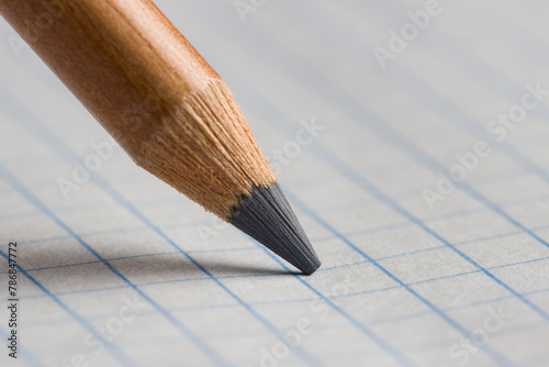 The tip of a pencil on a checkered paper in close-up.