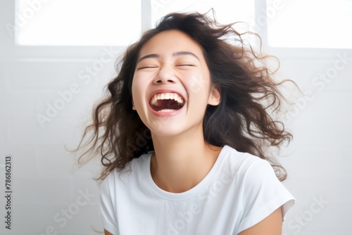 A beautiful Asian woman with long straight hair  whose skin is tan is wearing an all white shirt, and smiling with a face which is full of happiness in a white room. Generative AI.